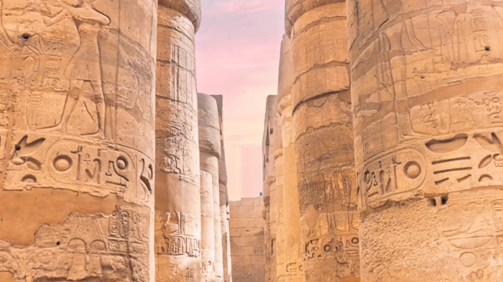 Visitor walking between hieroglyph-covered columns at Karnak Temple at dusk, Luxor