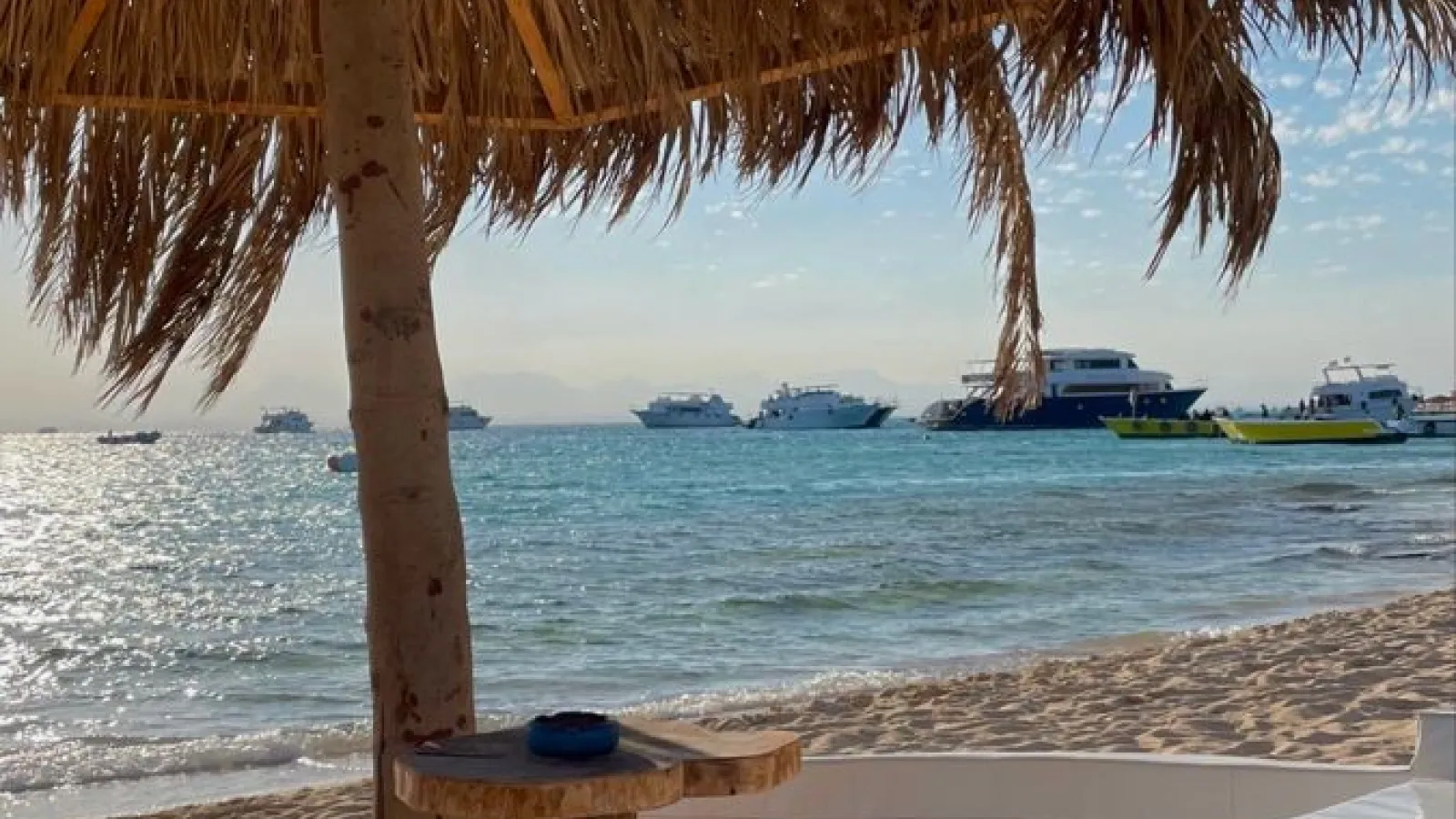 Thatched parasol on Paradise Island beach with excursion boats anchored offshore, Hurghada
