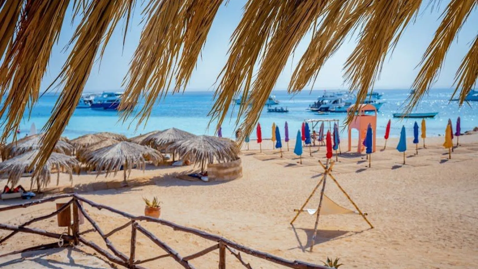 Paradise Island beach with thatch umbrellas, colourful parasols and boats at anchor, Hurghada