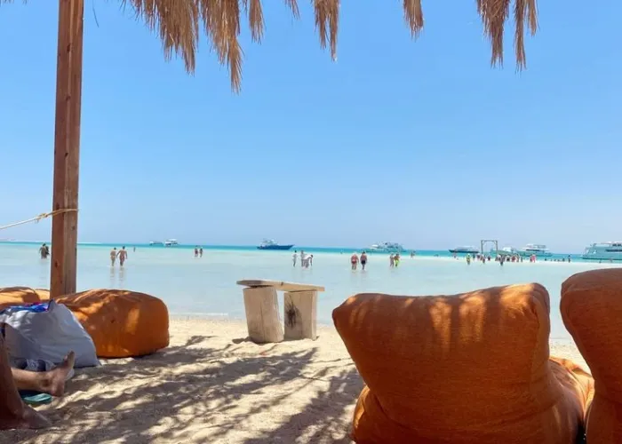 Orange beanbags under a straw parasol on Orange Bay beach with boats in the shallows, Giftun Island