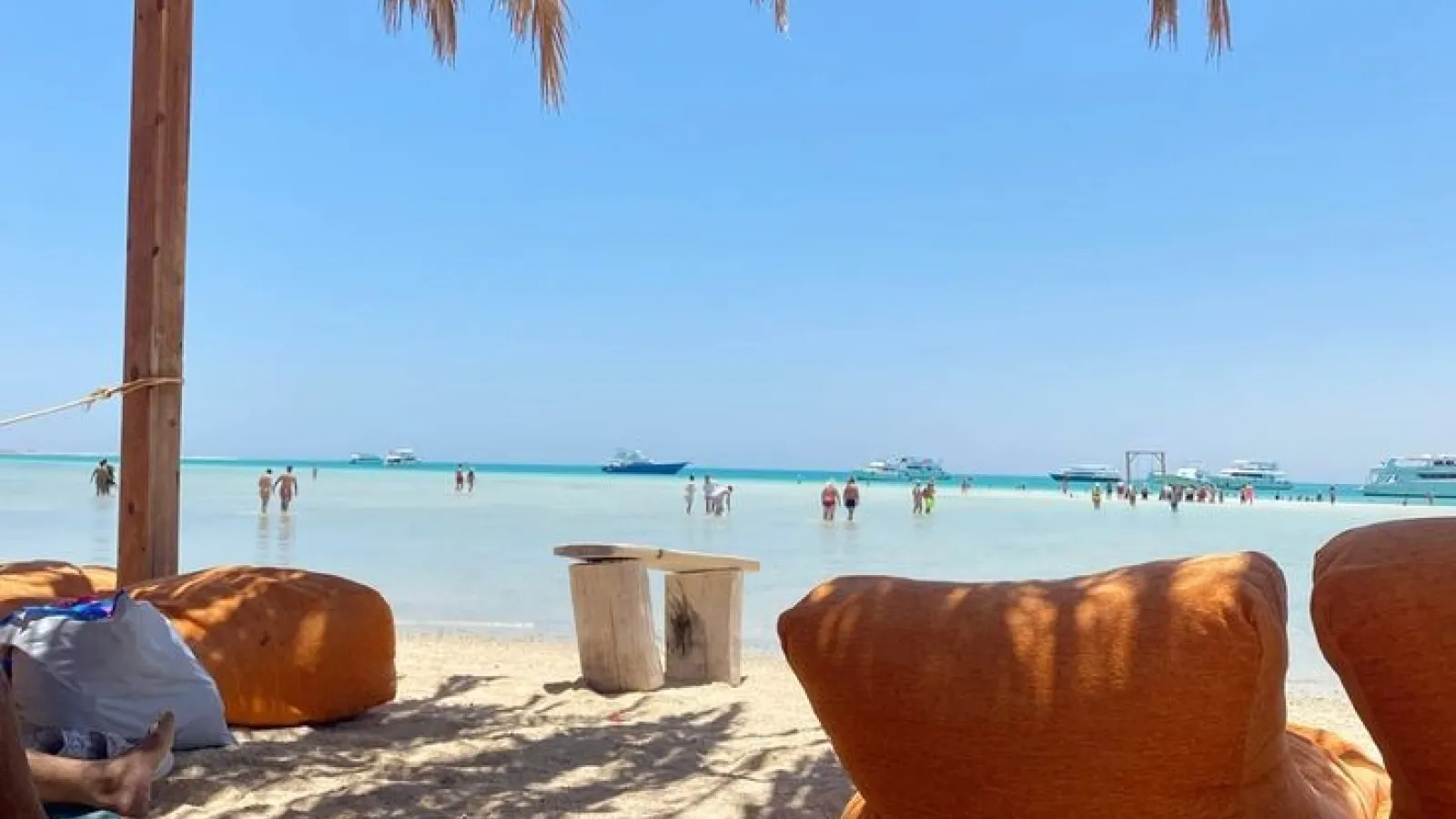 Orange beanbags under a straw parasol on Orange Bay beach with boats in the shallows, Giftun Island