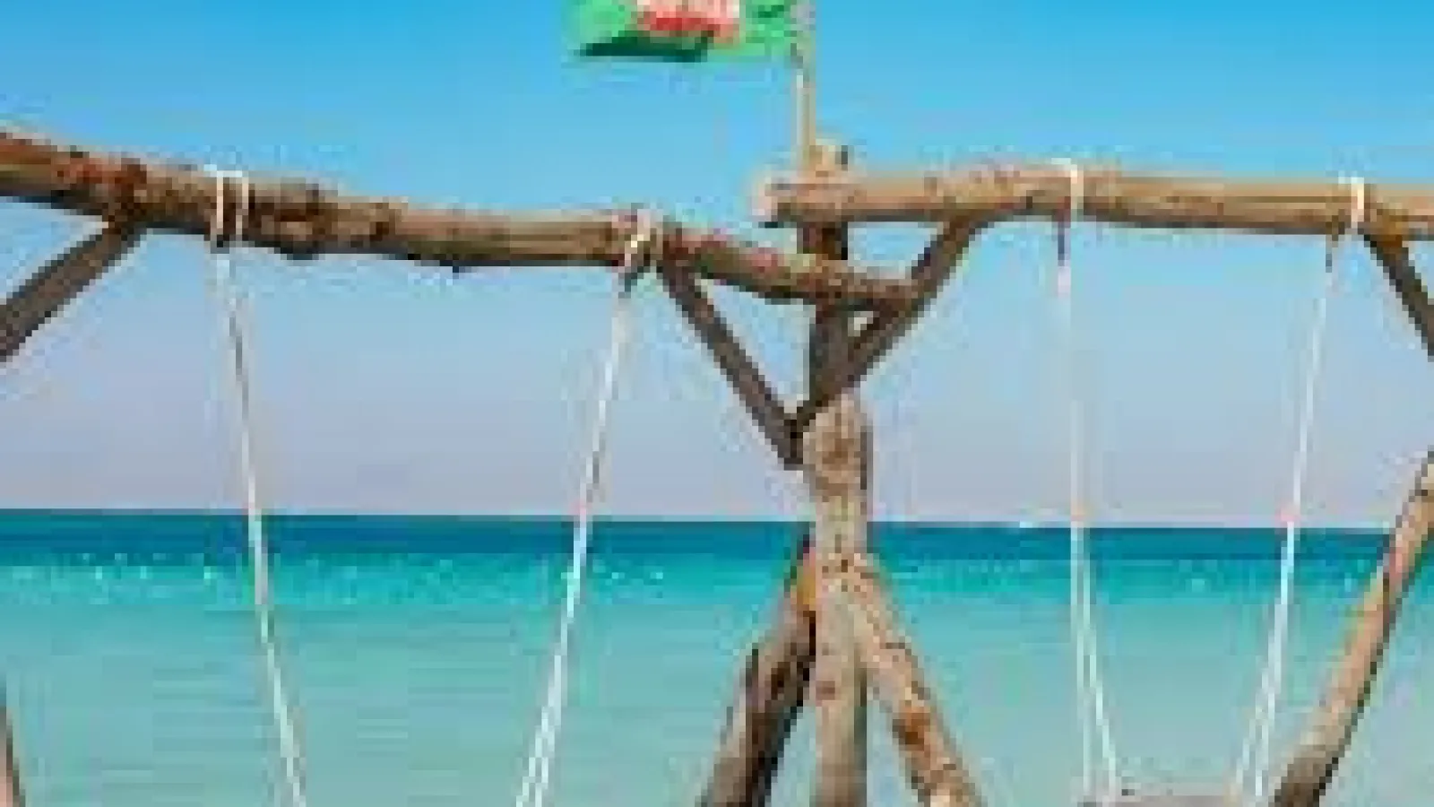 Wooden swing frame standing in the turquoise shallows of Hula Hula Island with a green flag