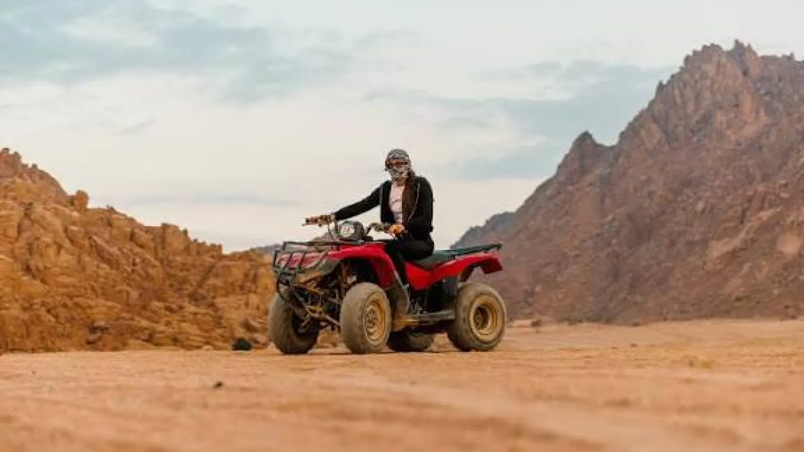 Rider in a headscarf on a red quad bike among the desert mountains near Hurghada