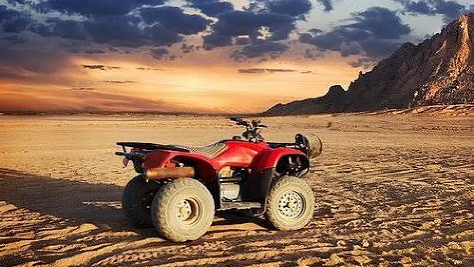 Red quad bike parked on rippled desert sand at sunset near Hurghada