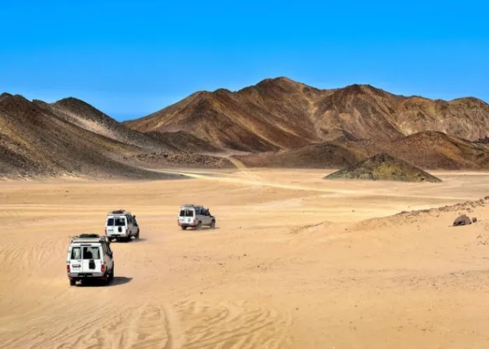 Three safari jeeps driving across the open desert towards the mountains near Hurghada
