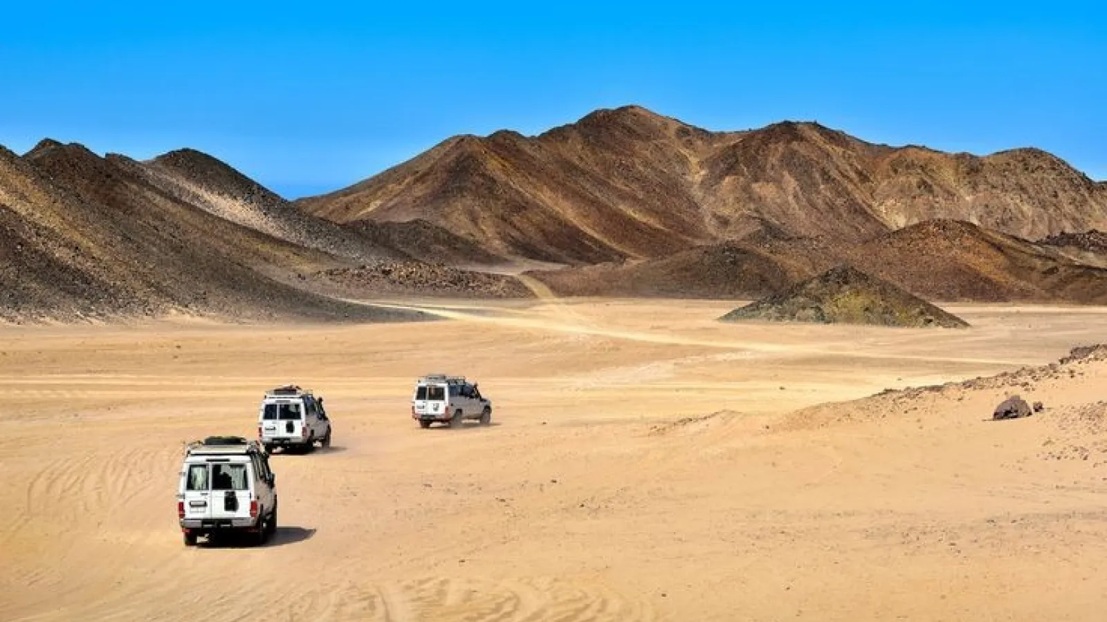 Three safari jeeps driving across the open desert towards the mountains near Hurghada