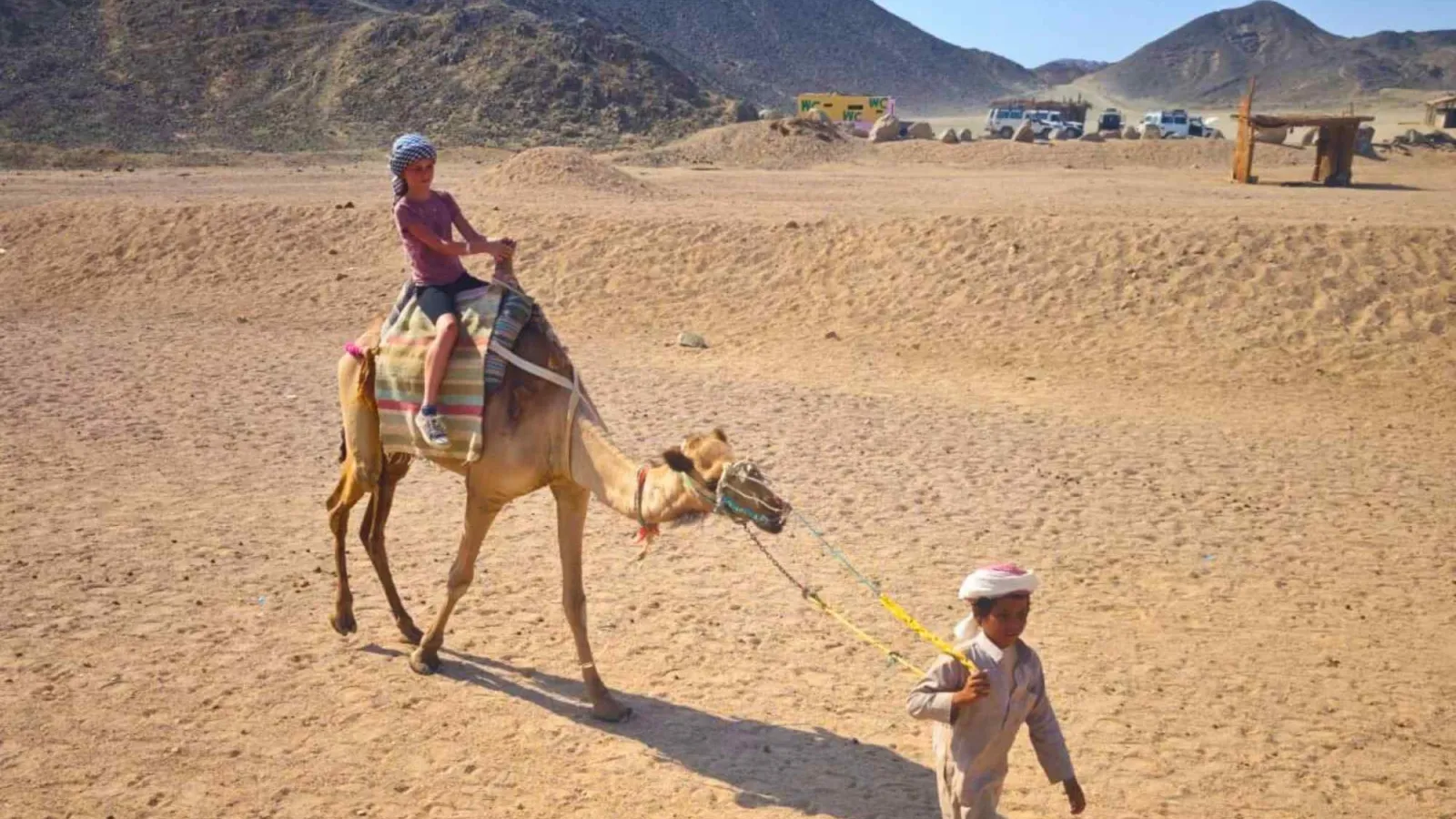 Child riding a camel led by a young Bedouin guide in the desert near Hurghada