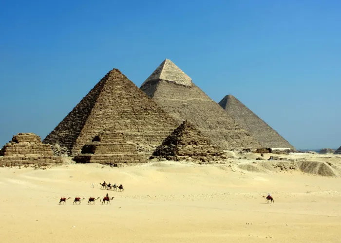 Camel caravan crossing the sand in front of the three Pyramids of Giza, Cairo