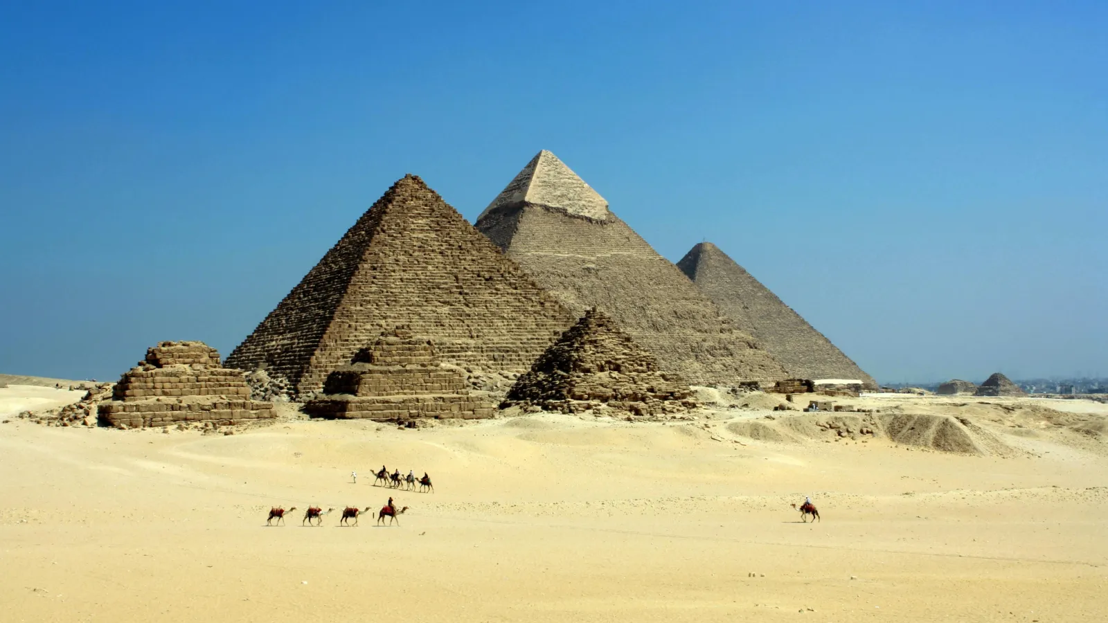 Camel caravan crossing the sand in front of the three Pyramids of Giza, Cairo